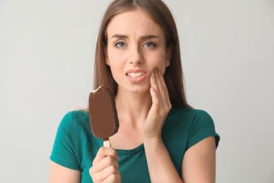 woman holding her jaw in pain while holding icecream bar