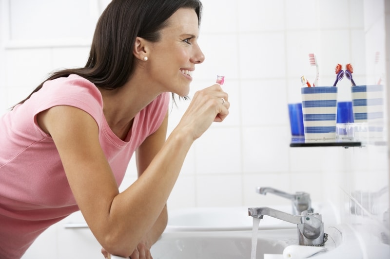 woman brushing her teeth in front of her bathroom mirror