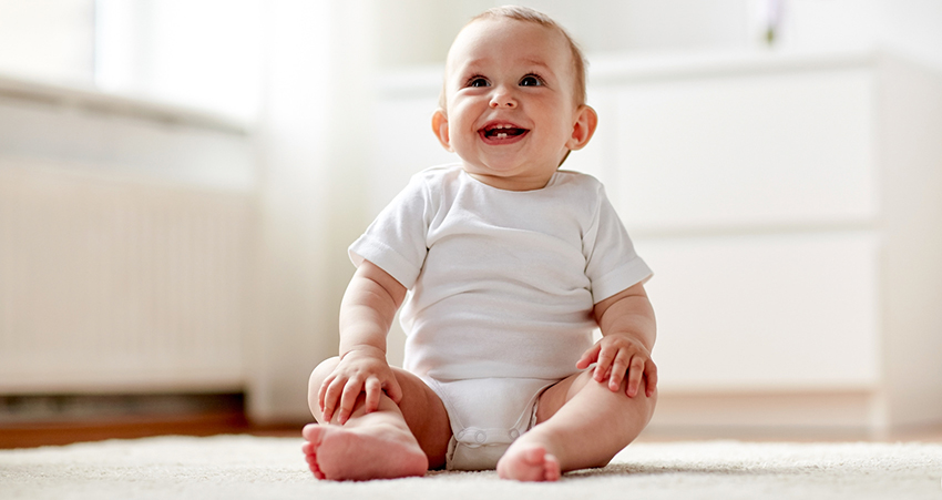 happy little baby boy or girl sitting on floor at home