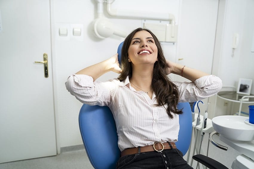 Gorgeous young adult woman enjoying her visit at dentist, relaxed in chair with hands behind her head. With Sedation Dentistry you never have to skip the dentist again. 