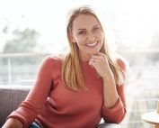 Woman smiling on couch in front of the sun